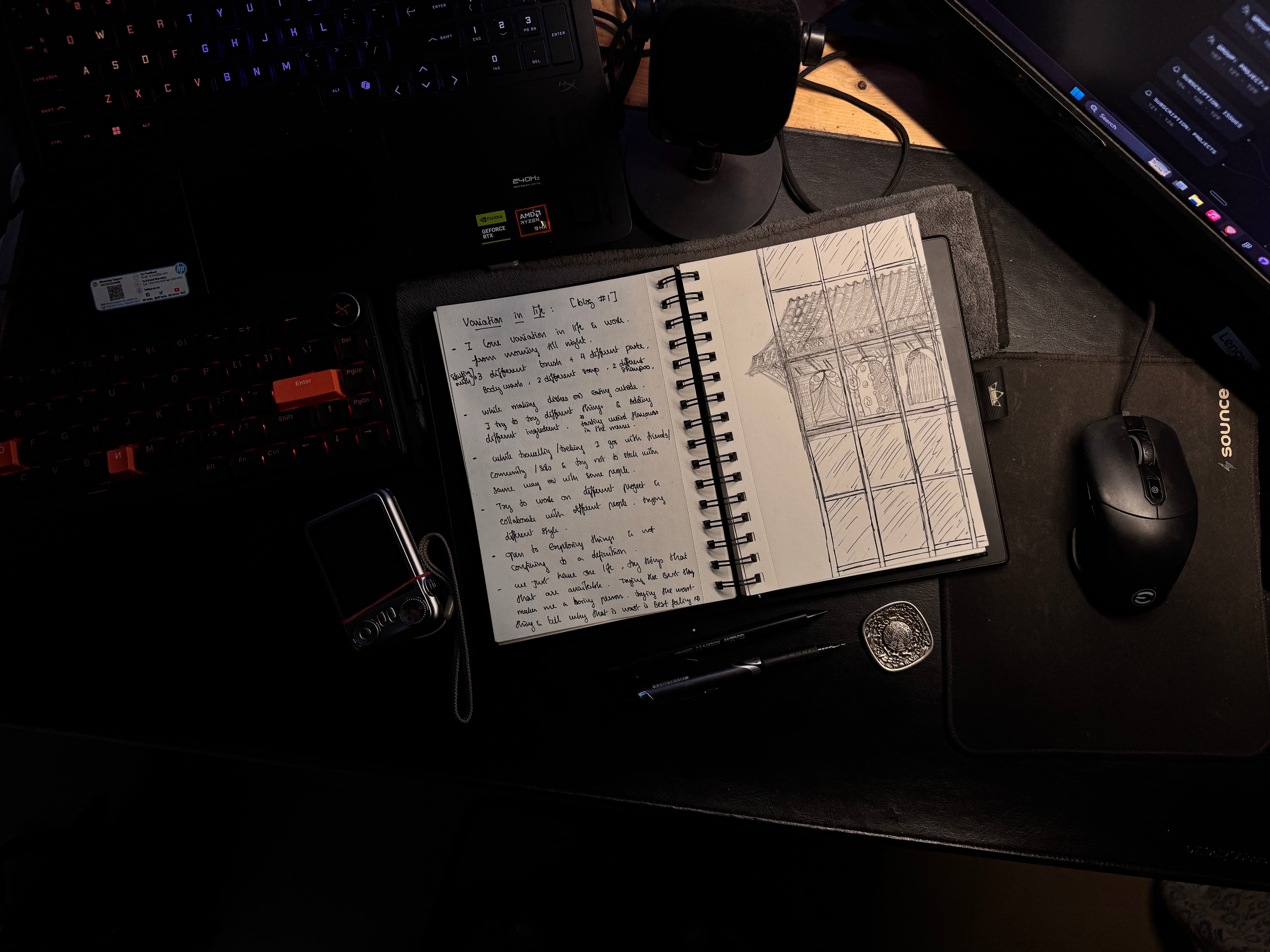 The same notebook on the desk, with a laptop, pens, and a mouse around it